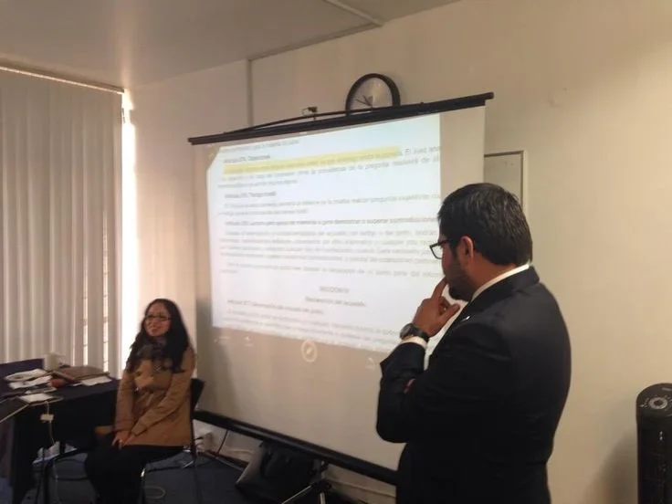 Hombre de pie junto a una exposición y una mujer sentada del otro lado